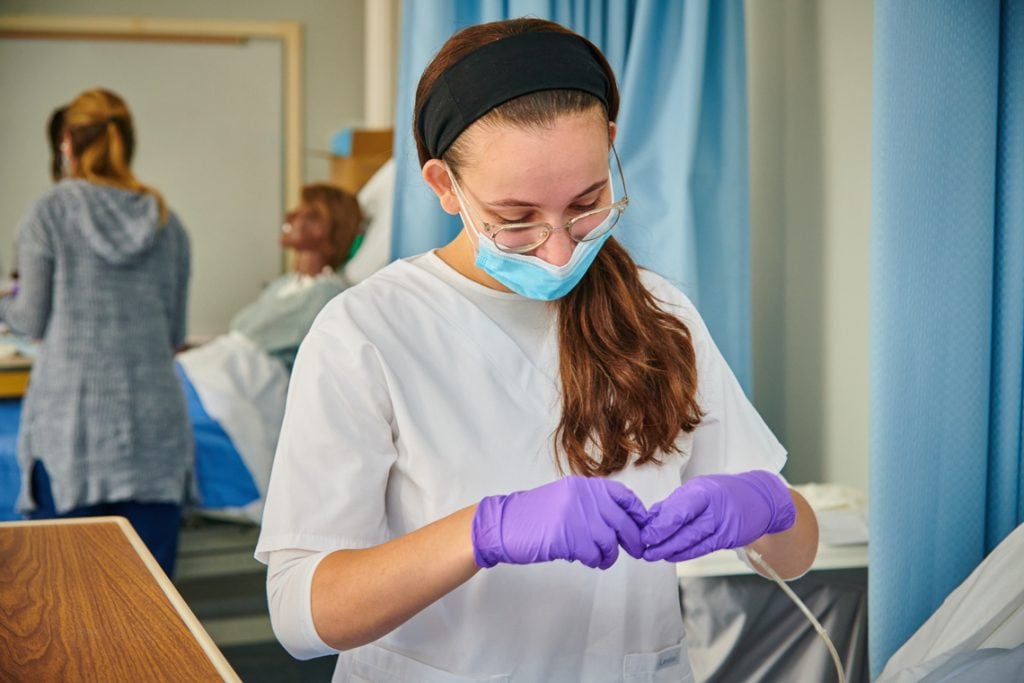 Nursing student in lab setting with purple gloves