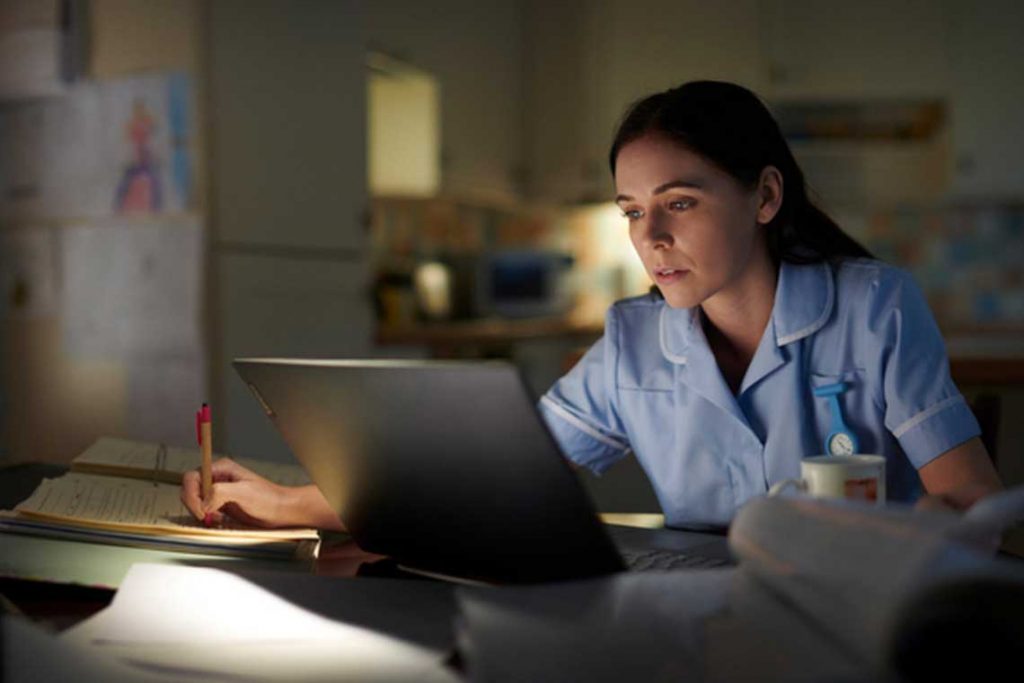 nurse sitting in dark room using laptop