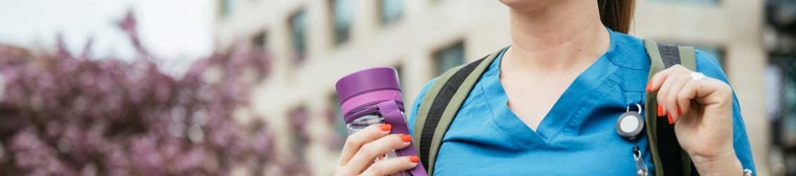 a travel nurse outside holding a bottle of water while smiling