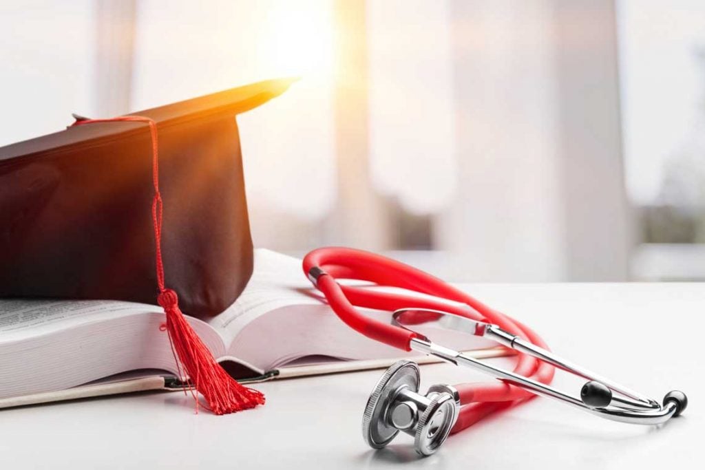 graduation cap on textbook next to stethoscope