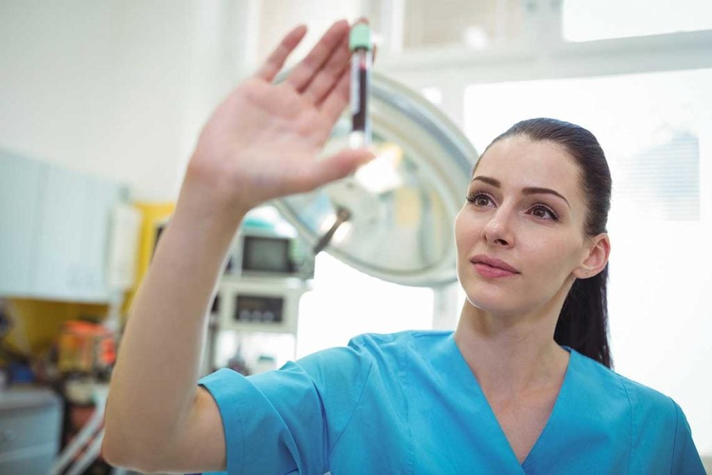 nurse holding up and looking at blood sample