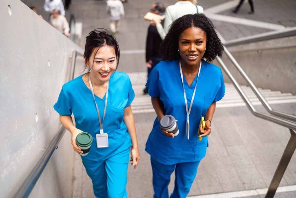 Two nurses walking up a flight of stairs smiling