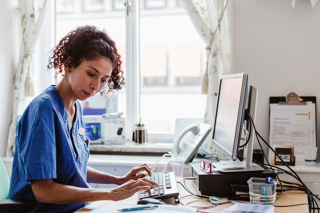 Current image: nurse in blue scrubs working at a computer